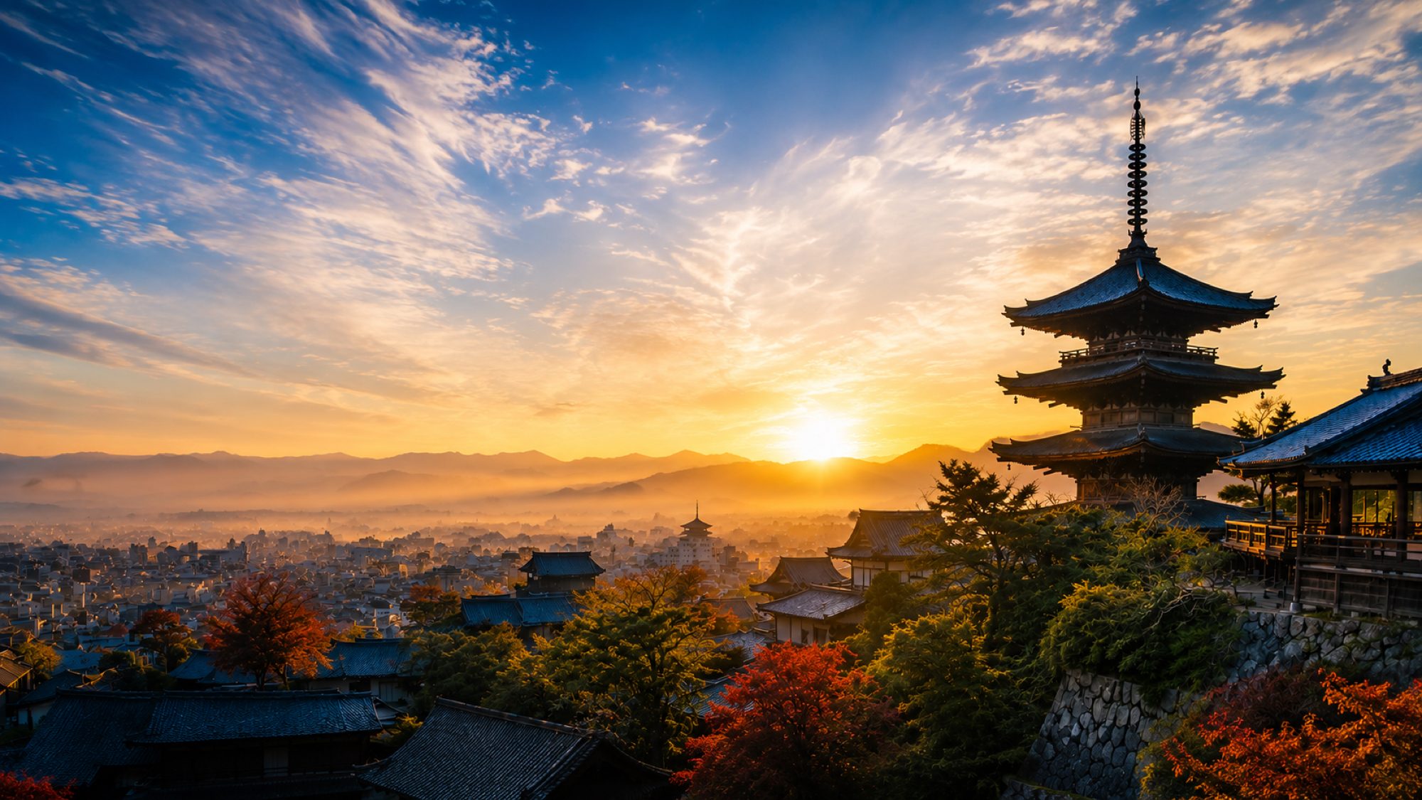 夜明けの京都。手前に社寺の甍と紅葉、右手に五重塔、その先に朝靄のかかった市街と山並みが広がる。