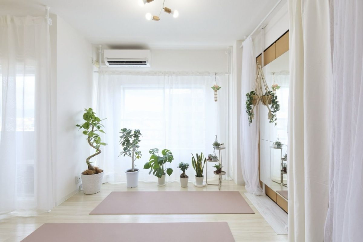 Interior of ITOHA YOGA SALON: yoga mats on a pale floor, framed by white curtains and house plants.